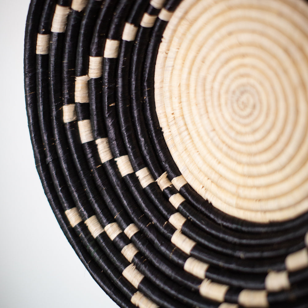 JustOne's black wall basket with tan designs, handwoven in Uganda
