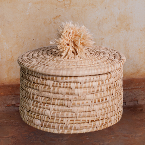 JustOne's tan basket and lid with a tan pompom handle, handcrafted in Uganda