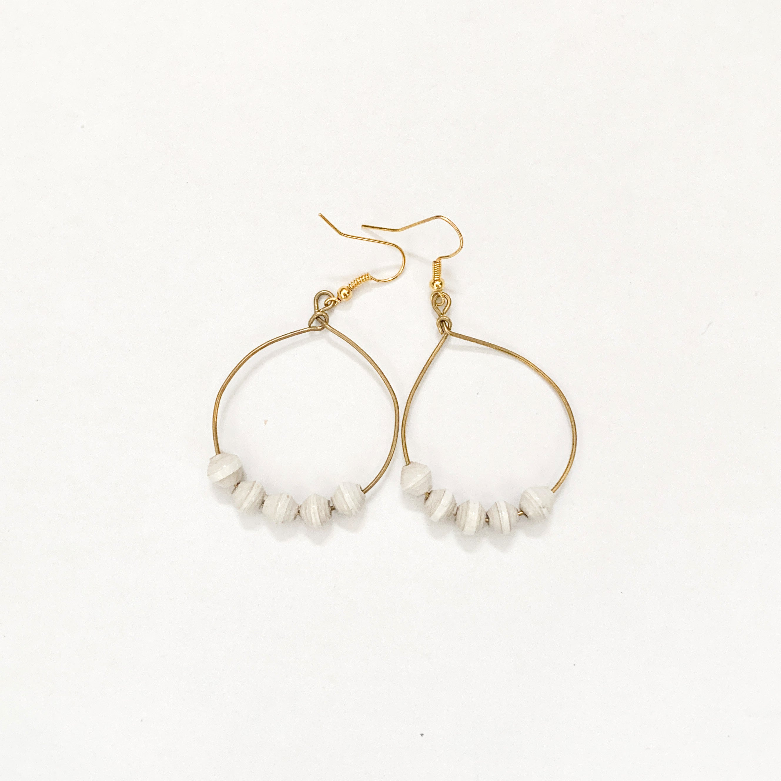 JustOne's brass hoop earrings with five white paper beads on the bottom of the hoop, handcrafted in Uganda