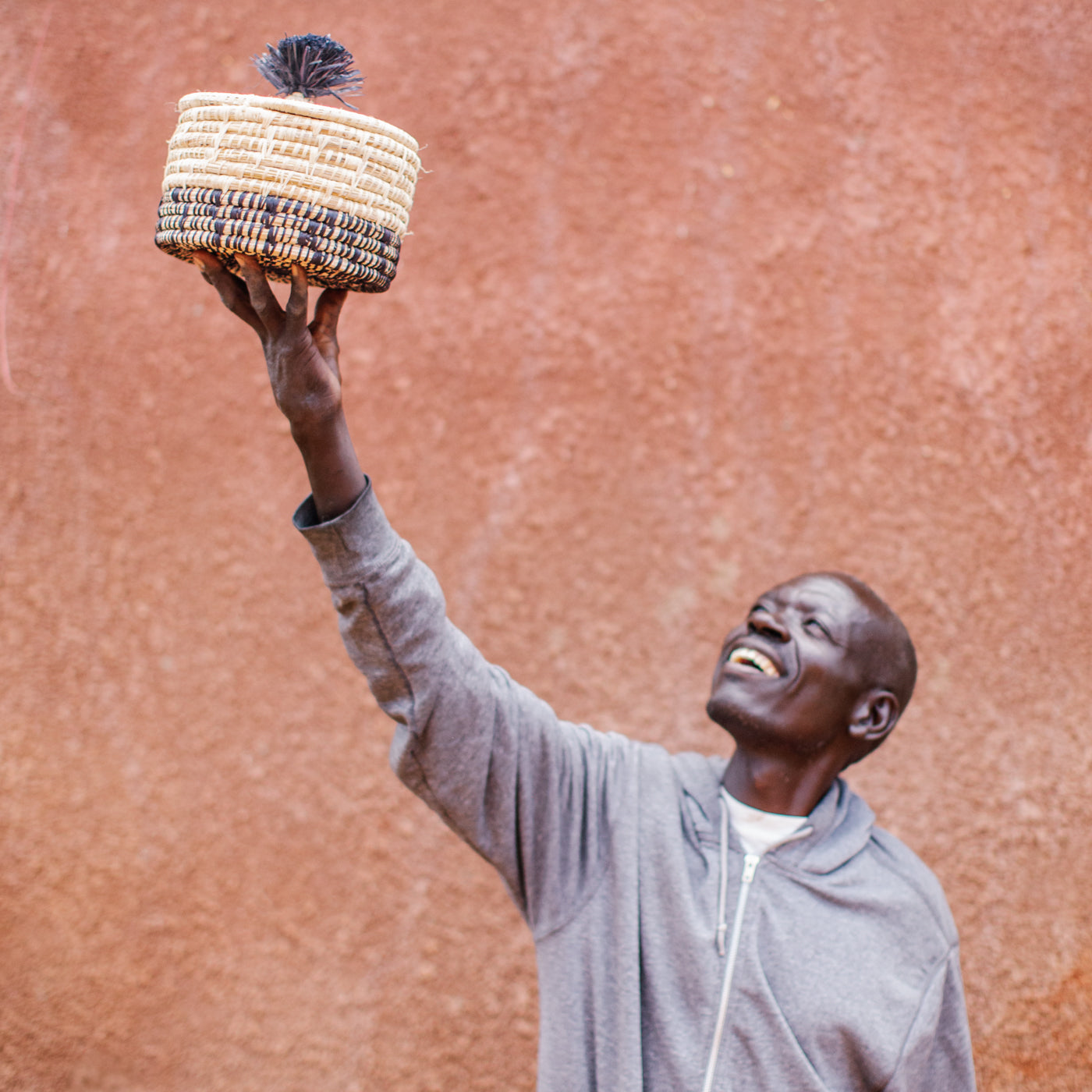 JustOne's natural basket with black details on bottom and lid with a black pompom handle, handcrafted in Uganda
