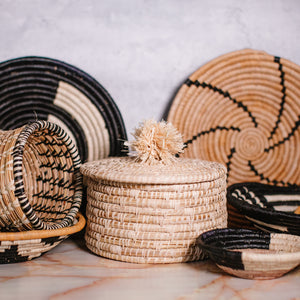 JustOne's tan basket and lid with a tan pompom handle, handcrafted in Uganda