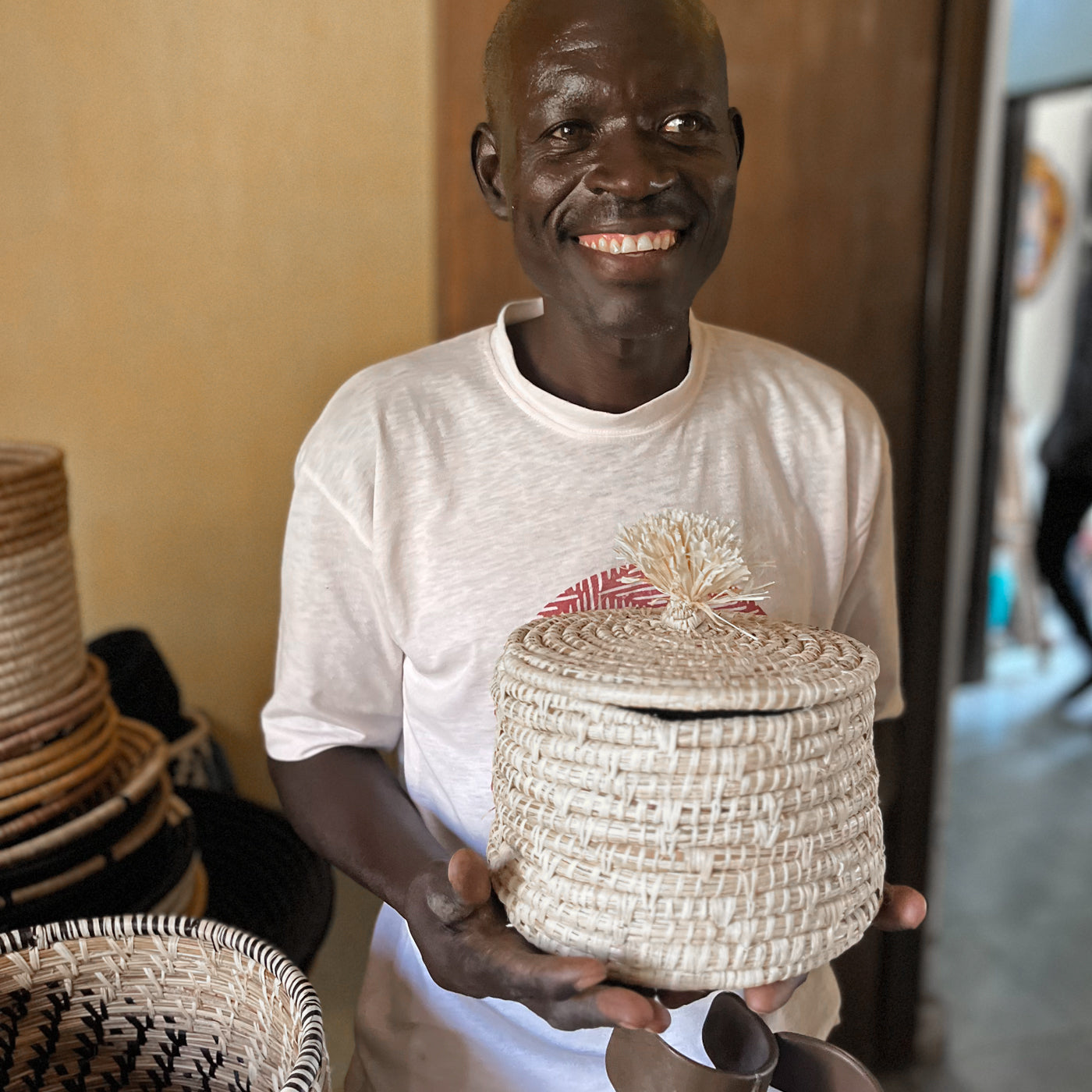 JustOne's tan basket and lid with a tan pompom handle, handcrafted in Uganda