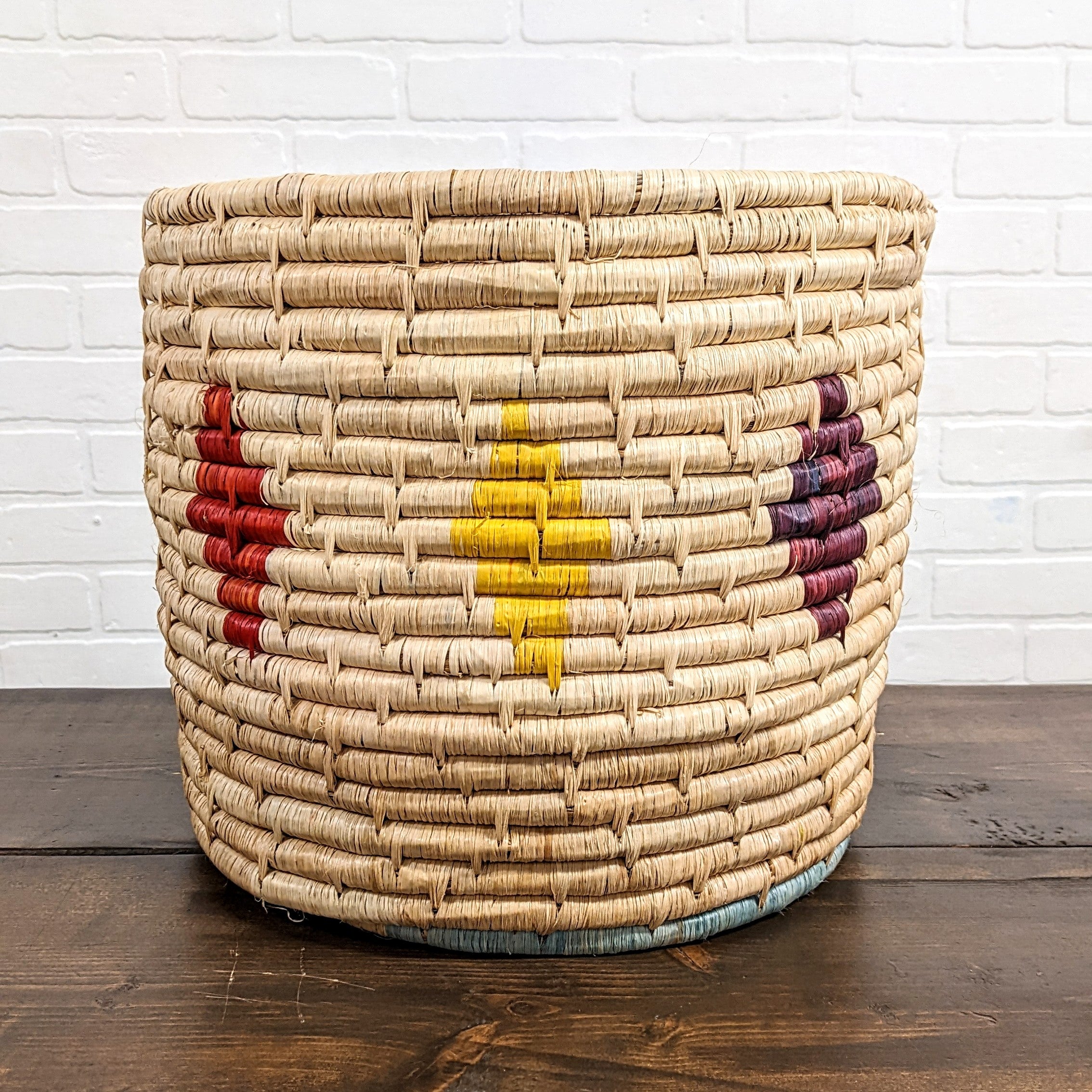 JustOne's large, deep tan basket with red, yellow and purpe diamonds around the outside, handwoven in Uganda