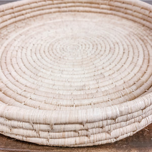 JusrtOne's large, shallow, round basket in tan, handwoven in Uganda
