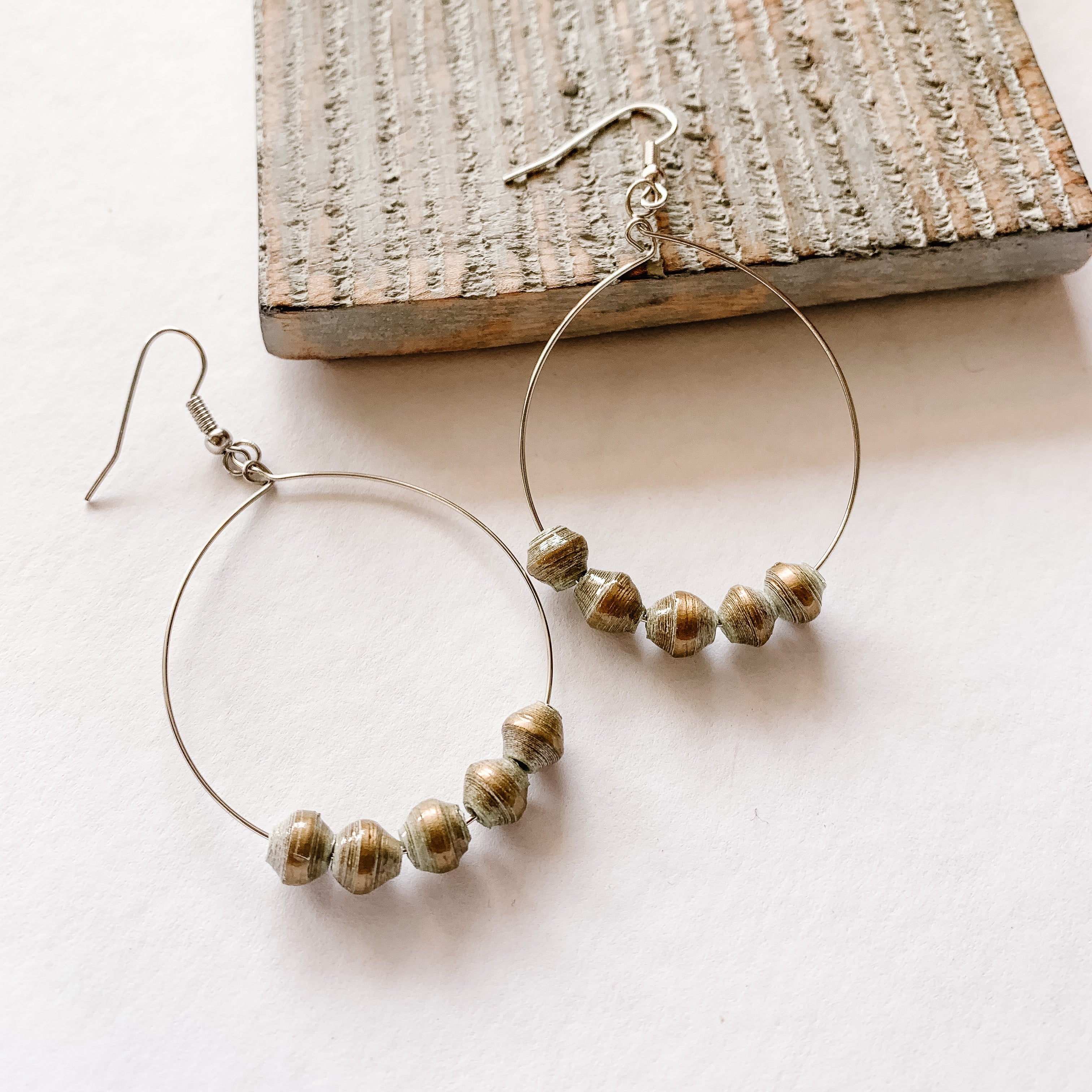 JustOne's silver hoop earrings with five gold paper beads on the bottom of the hoop, handcrafted in Uganda